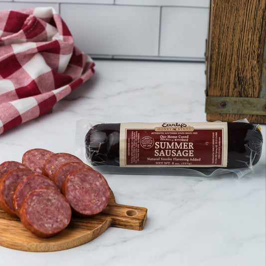 Sliced summer sausage on a wooden board with a package of summer sausage and a checkered cloth in the background.